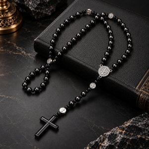Chapelet Saint-Benoît noir avec médaille argentée et crucifix, présenté près d’une Bible et d’une bougie.