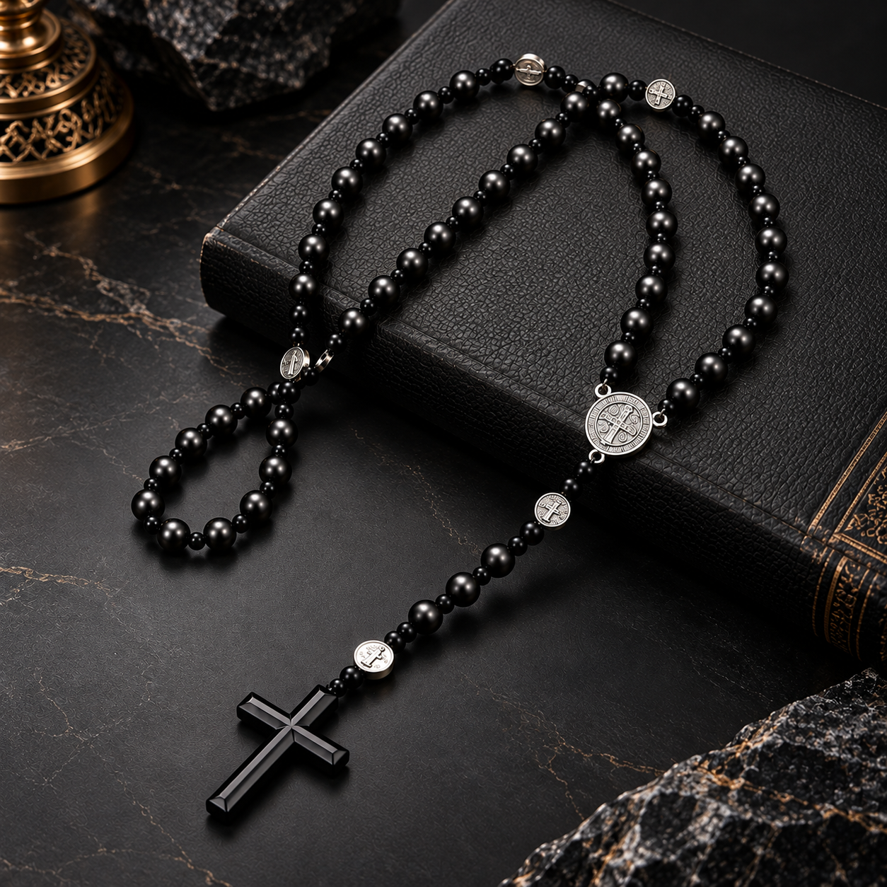 Chapelet Saint-Benoît noir avec médaille argentée et crucifix, présenté près d’une Bible et d’une bougie.
